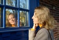 A young woman looks at her reflection on the glass of a blue door Royalty Free Stock Photo