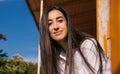 A young woman looks out from the balcony.The bright sun shines on the girl. Beautiful brunette girl enjoys the sun