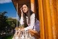 A young woman looks out from the balcony.The bright sun shines on the girl. Beautiful brunette girl enjoys the sun