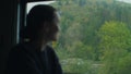 Young woman looks out of the train window on mountains view. Passenger train passes mountain villages, Beautiful nature