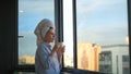 Young woman looks out window and drinks coffee in morning. Concept. Beautiful woman starts day with cup of coffee and