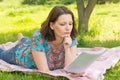 A young woman looks at the paper lying on the meadow in the park