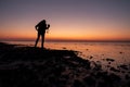 Young woman looks at the water with the camera in hand, during sunset