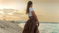 Young woman lost in thought, holding a fluttering silk scarf and staring at the ocean horizon during sunset at the beach Royalty Free Stock Photo