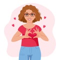 A young woman in love in glasses with a joyful expression on her face shows a heart with her hands. Emotions and gestures.