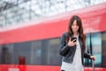 Young woman with luggage looking oh cellphone at a train station. Caucasiam tourist waiting her express train while her Royalty Free Stock Photo