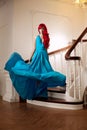 Young woman with luxurious long beautiful red hair in a blue fashionable evening dress in the rich interior. Royalty Free Stock Photo