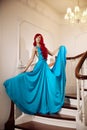 Young woman with luxurious long beautiful red hair in a blue fashionable evening dress in the rich interior. Royalty Free Stock Photo