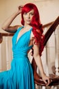 Young woman with luxurious long beautiful red hair in a blue fashionable evening dress in the rich interior. Royalty Free Stock Photo