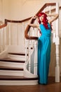 Young woman with luxurious long beautiful red hair in a blue fashionable evening dress in the rich interior. Royalty Free Stock Photo