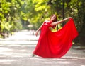 Young woman in luxury long red dress dancing, jumping in city park Royalty Free Stock Photo