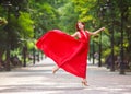 Young woman in luxury long red dress dancing, jumping in city park Royalty Free Stock Photo