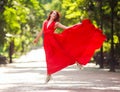 Young woman in luxury long red dress dancing, jumping in city park Royalty Free Stock Photo