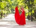 Young woman in luxury long red dress dancing, jumping in city park Royalty Free Stock Photo