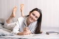 Young woman lying on the bed at home bedroom and writing into diary or planning her day, making schedule for tomorrow. Concept - r Royalty Free Stock Photo