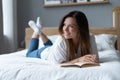 Young woman lying on bed and reading book at home. Royalty Free Stock Photo