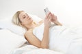 Young woman lying in the bed with a smartphone. Beautiful blond awakening girl. Morning in the bedroom, daylight from Royalty Free Stock Photo