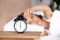 Young woman lying in bed, woken by alarm signal, turning off clock Royalty Free Stock Photo
