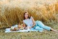 A young woman is lying on a blanket against a background of wheat. A lady on a picnic with milk, bread and fruit in nature at