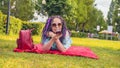 Young woman lying on a blanket records a voice message using a smartphone in the park. Happy girl lying on the grass and