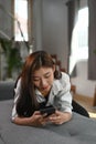 A young woman is lying on couch and using smart phone browsing internet. Royalty Free Stock Photo