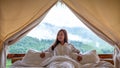 A young woman lying down on a white bed in the morning with a beautiful nature view outside the tent Royalty Free Stock Photo