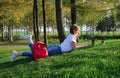 Young woman lying on green grass in city park working on laptop. Freelance business concept, student studying outdoors Royalty Free Stock Photo