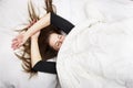 Young woman is lying in her bed with closed eyes, smiling under her blanket after a restful sleep.