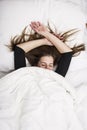 Young woman is lying in her bed with closed eyes, smiling under her blanket after a restful sleep.