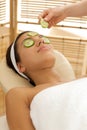 Young woman lying on massage table with cucumber slice being placed over eye Royalty Free Stock Photo