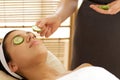 Young woman lying on massage table with cucumber slice being placed over eye Royalty Free Stock Photo