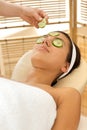 Young woman lying on massage table with cucumber slice being placed over eye Royalty Free Stock Photo