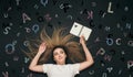 Young woman lying with pencil and notebook top view on black studio background with scattered letters written and chalk shaded on Royalty Free Stock Photo