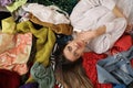 Young woman lying on pile of clothes, top view. Fast fashion concept