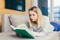 Young woman lying on sofa at home and reading a book. student girl studying lessons. female relaxes indoors on a comfor Royalty Free Stock Photo