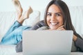 Young woman lying on sofa and using laptop at home - Happy girl surfing online with her computer while smiling at camera Royalty Free Stock Photo