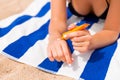 Young woman is lying on striped towel on the sand at the beach and applying sun cream on her hand Royalty Free Stock Photo