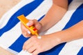 Young woman is lying on striped towel on the sand at the beach and applying sun cream on her hand Royalty Free Stock Photo