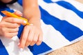 Young woman is lying on striped towel on the sand at the beach and applying sun cream on her hand Royalty Free Stock Photo