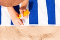 Young woman is lying on striped towel on the sand at the beach and applying sun cream on her hand Royalty Free Stock Photo