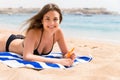 Young woman is lying on the towel at the beach and applying sunbclock from the tube on her hand Royalty Free Stock Photo