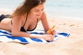 Young woman is lying on the towel at the beach and applying sunbclock from the tube on her hand Royalty Free Stock Photo