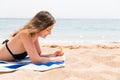 Young woman is lying on the towel at the beach and applying sunbclock from the tube on her hand Royalty Free Stock Photo