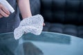 Young woman maid in apron is cleaning, wiping down office glass table surface with spray bottle cleaner, wet rag, close up, Royalty Free Stock Photo