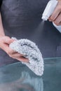 Young woman maid in apron is cleaning, wiping down office glass table surface with spray bottle cleaner, wet rag, close up, Royalty Free Stock Photo