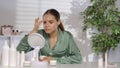 A young woman without makeup applying white cream on problem skin areas of the face. A woman in green silk pajamas Royalty Free Stock Photo