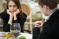 Young woman making an exasperated expression gesture on a bad date at the restaurant. Man looks at his watch. Royalty Free Stock Photo
