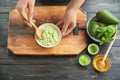 Young woman making nourishing mask with avocado at table