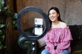 Young woman making photo or video content for social media with smartphone and light of ring lamp. Beauty blogger smiles Royalty Free Stock Photo