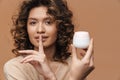 Young woman making silence gesture while showing facial cream Royalty Free Stock Photo